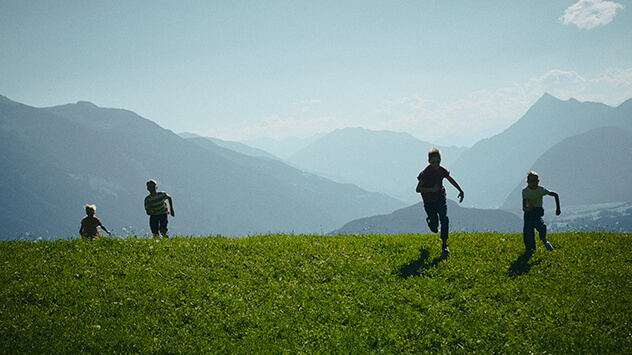 Herumtollende Kinder auf einer grünen Bergwiese in Tirol