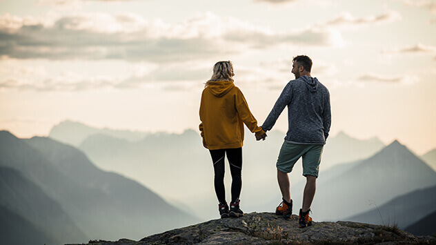 Mann und Frau stehend händchenhaltend auf einer Bergspitze im Paznaun