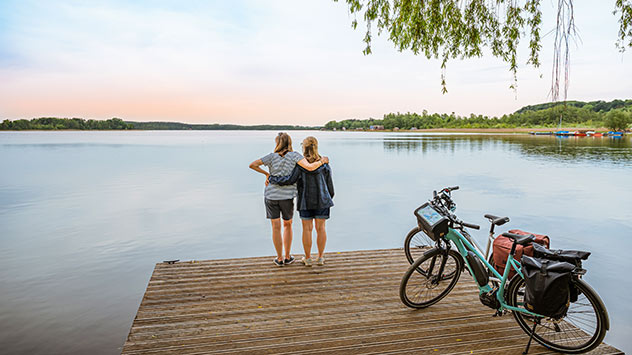 Zwei Frauen bei einer Pause vom Radfahren auf einem Steg am See