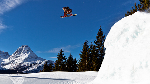 Snowboarder fliegt bei einem Sprung über die Piste